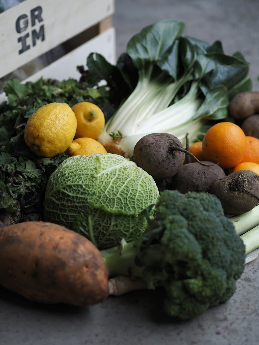 Varietà di frutta e verdura biologica fresca disposta su una superficie di cemento grigio.